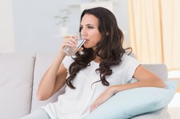 Pretty brunette drinking water on couch at home in the living room-1
