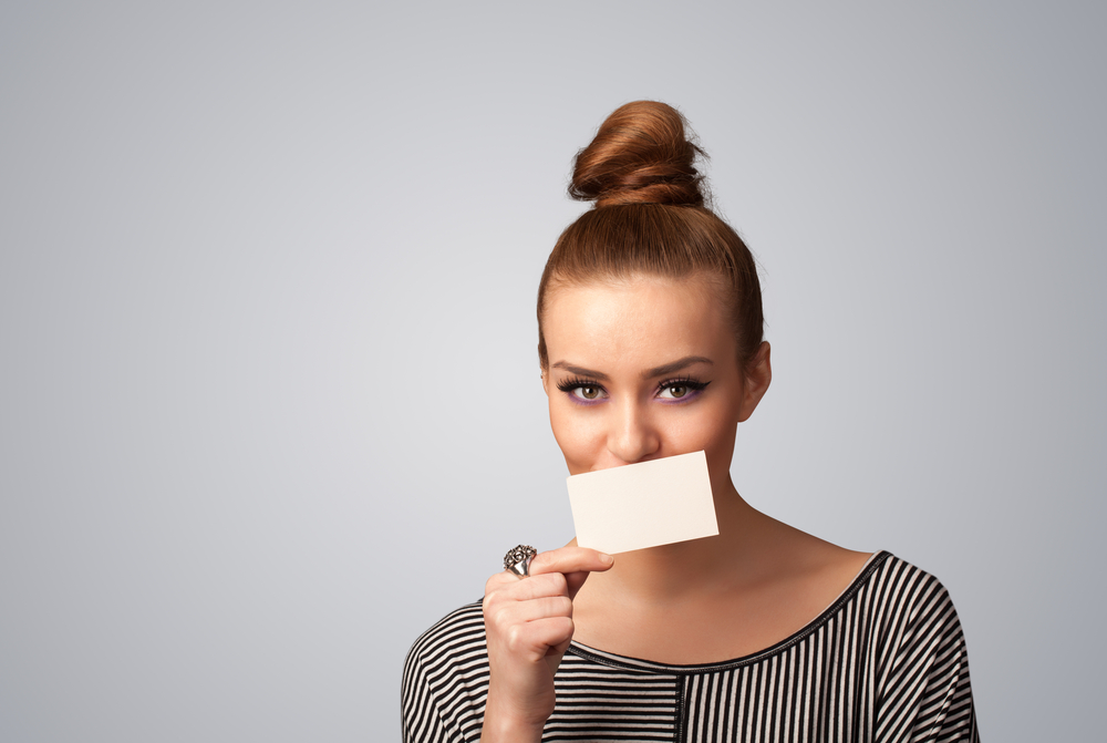 Cute girl holding white card at front of her lips with copy space on gradient background